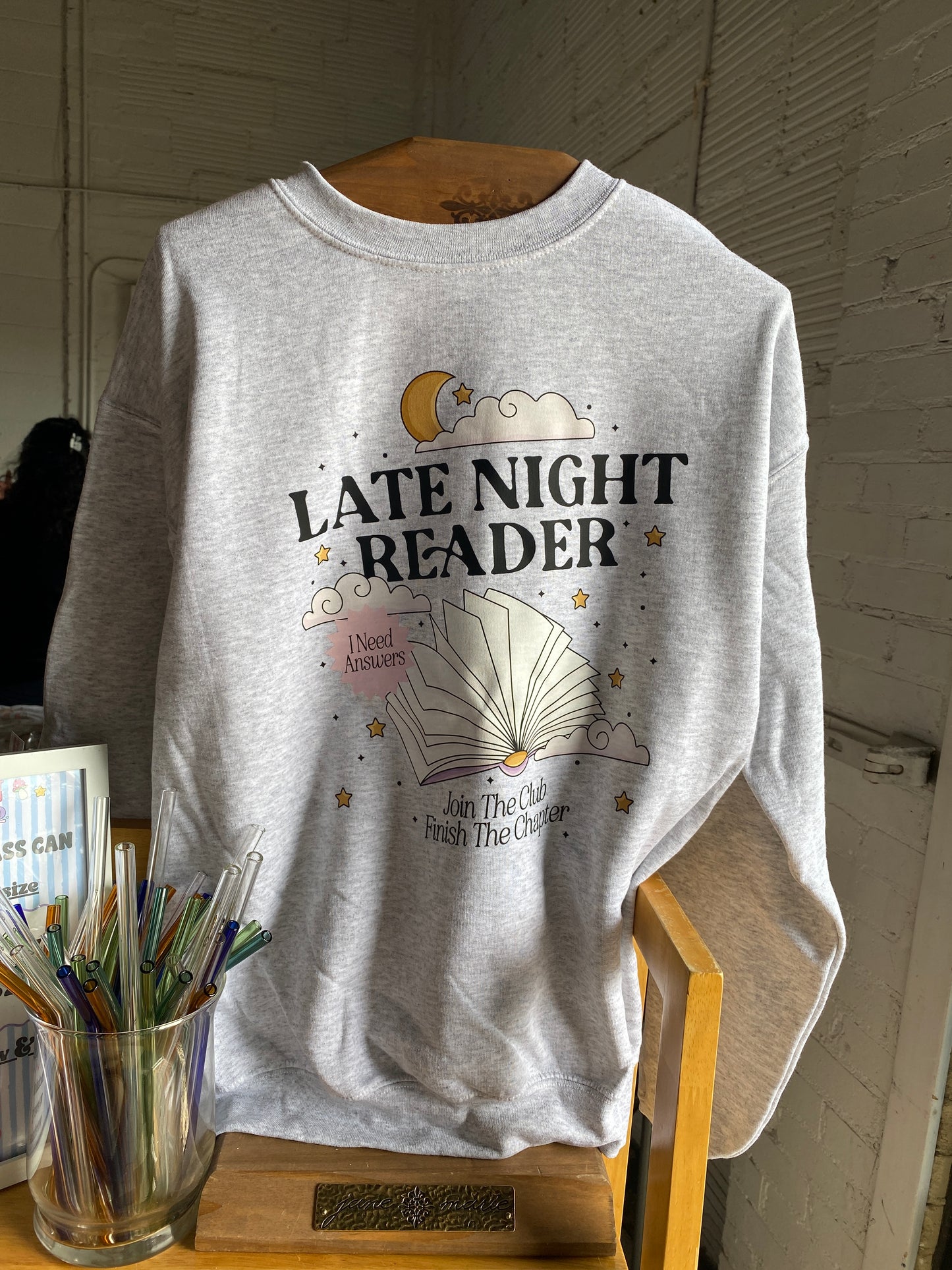 Gray tank top with 'Late Night Reader' text and graphics on a wooden surface.